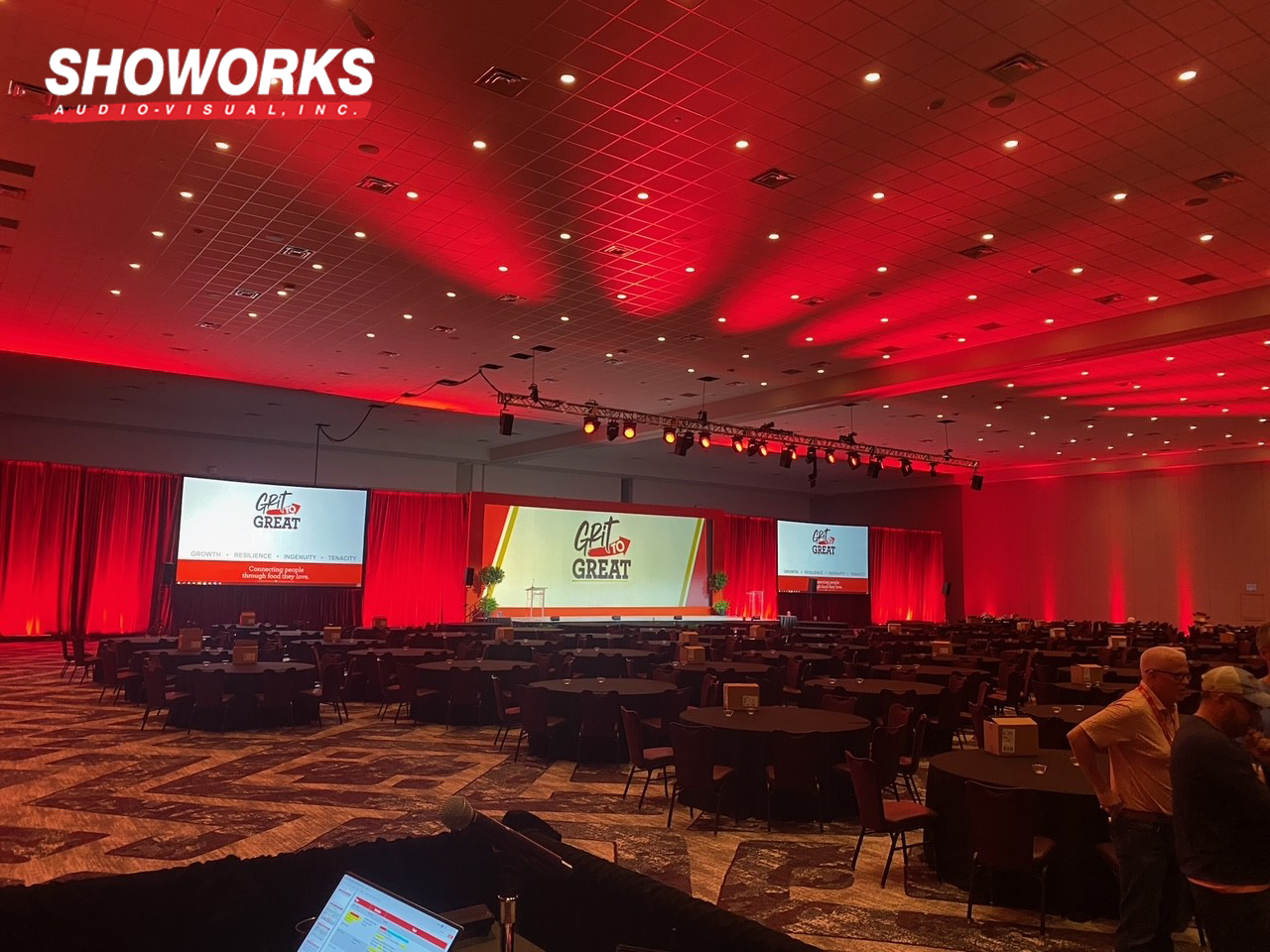 Large corporate event space with red lighting and full AV setup by Showorks Audio-Visual, Inc.