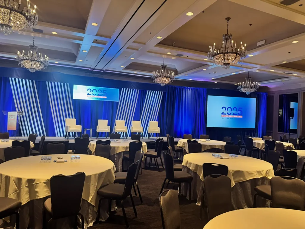 Showorks AV conference stage with blue draping, presentation screens, panel chairs, and banquet tables.