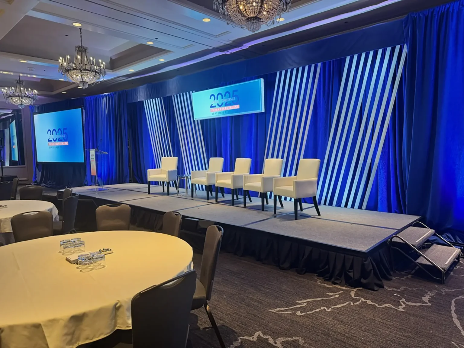 Showorks AV panel stage with six chairs, blue striped curtains, and two presentation screens.