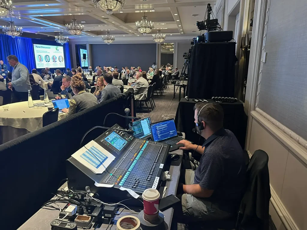 Showorks AV technician operates the audio mixing console during a conference panel as attendees watch.