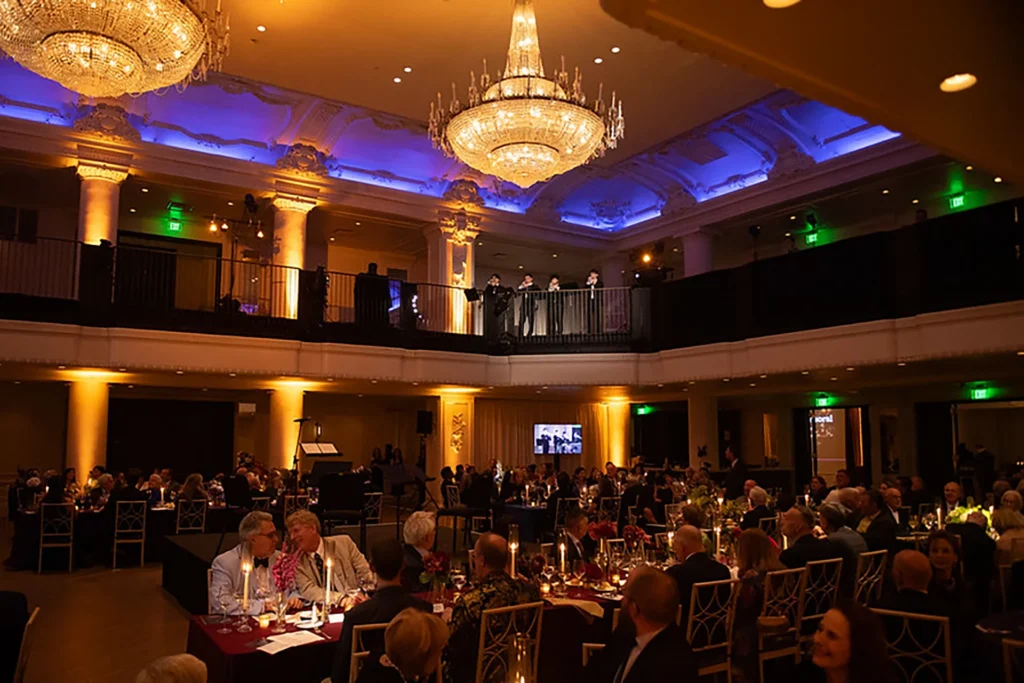 Showorks AV provides warm lighting for a seated gala with musicians performing on an upper balcony.