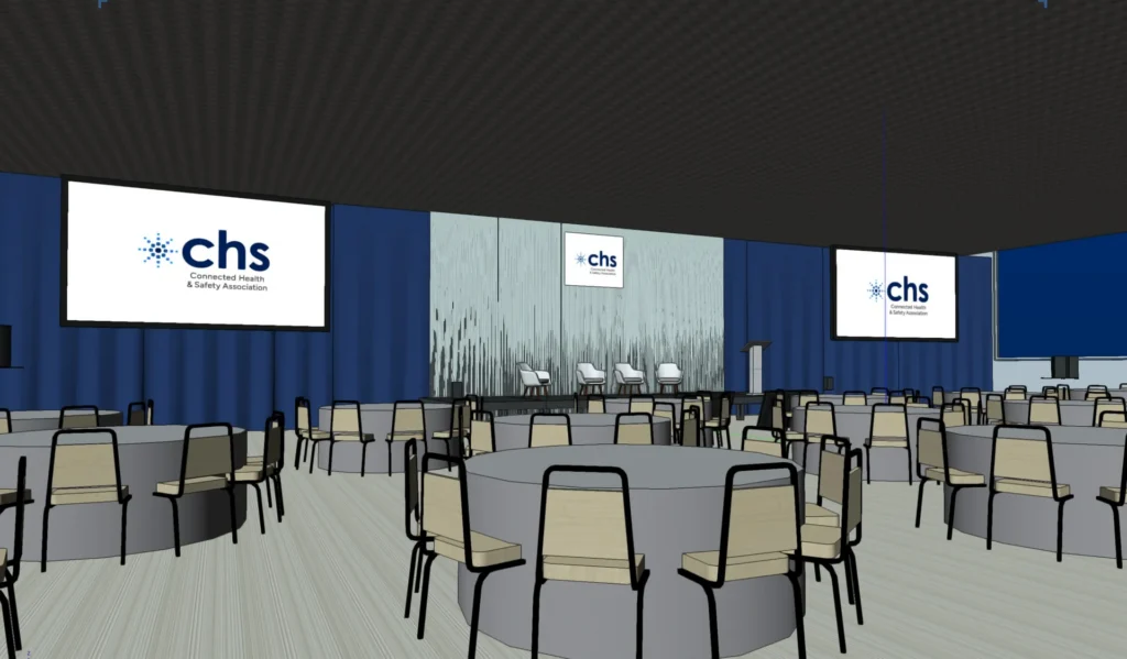 Conference room with round tables and chairs facing a stage with four chairs and three screens displaying the chs logo.