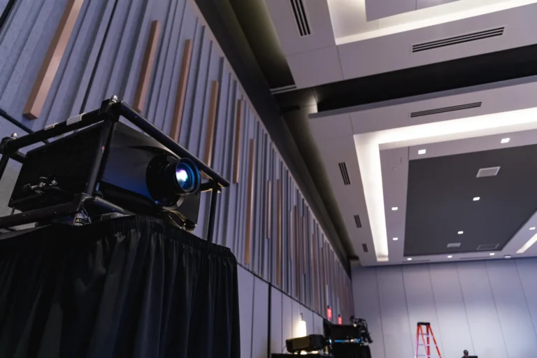 Projector set on a black draped stand in a conference room with a ladder in the background.